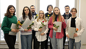 Es sind alle acht Stipendiaten zu sehen mit Urkunde und Blumen in der Hand.
