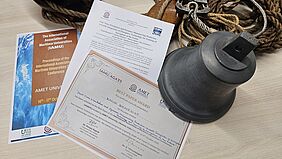 best paper Die Auszeichnungsurkunde liegt auf dem Titelblatt des Konferenzbeitrags und dem Titelblatt des Konferenzbandes. Dahinter befinden sich Taue und eine Schiffsglocke.