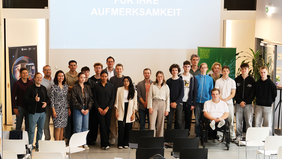 Group photo of about 25 people including students, jury members, and university staff. They are standing together in the InnovationPort Wismar presentation space in front of a screen with the words "Für Ihre Aufmerksamkeit" (“Thank you for your attention”).
