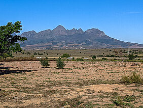 Es ist ein trockenes, mit nur wenigen grasbüscheln versehenes Land zu shen. Im Hintergrund ragen Berge auf.