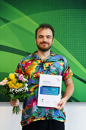 Leon Kreft erhält Bachelorpreis Leon Kreft präsentiert Urkunde und Blumenstrauß nach der Ehrung seiner Bachelorarbeit.