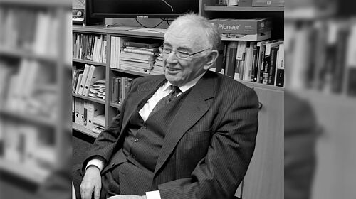 Dr. George F. Page sitzt vor einem Bücherregal im einem Büro auf dem Campus der Hochschule Wismar. 