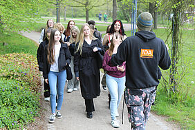 Ein Student läuft rückwärts ins Bild und erklärt Schülerinnen etwas, die ihm folgen.